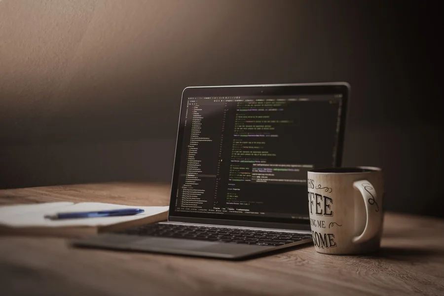 Programming Student Workspace A person typing code on a laptop while sitting at a wooden desk with a coffee mug