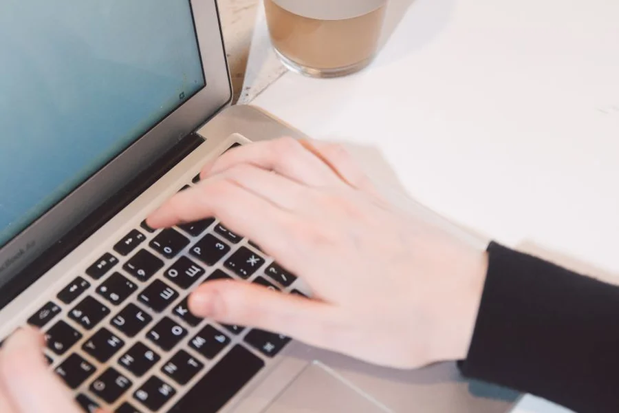 Writing Prompts in Action A person typing text prompts into a laptop on a wooden desk with a coffee mug